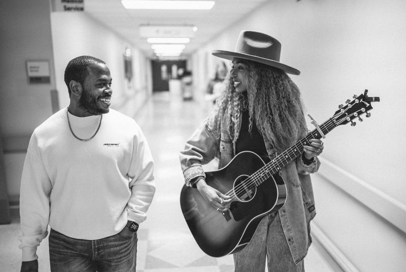 Shared grin as she plays guitar down a monochrome hallway