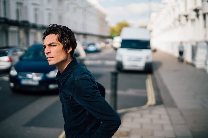 A tight portrait, dark denim jacket, a blurred London street behind him