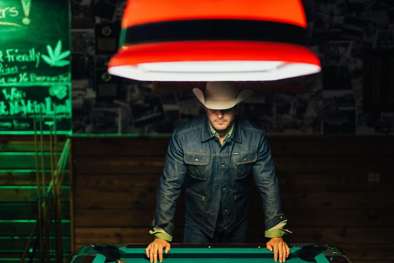 Leaning on a pool table under a red lamp, green neon