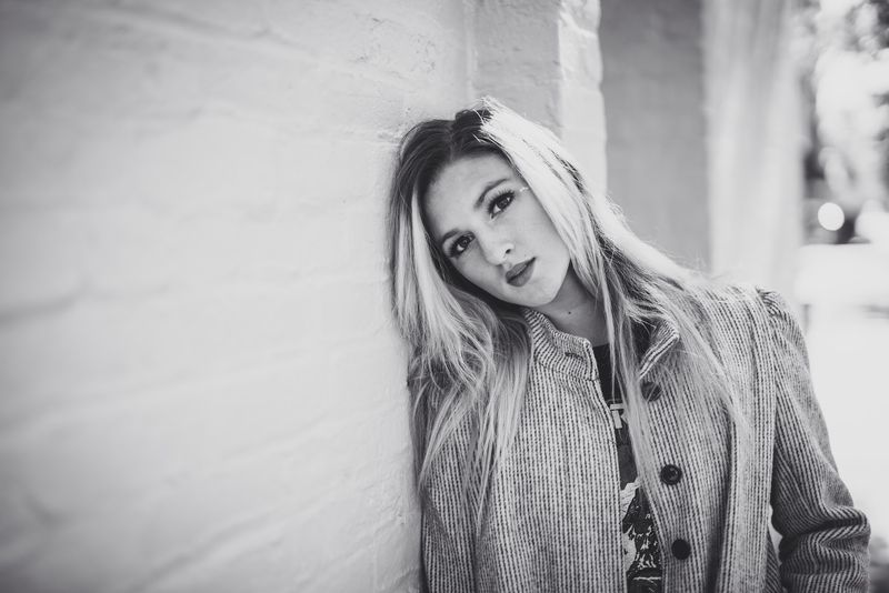Black and white, a head tilted against a white wall, a grey cardigan, a direct gaze
