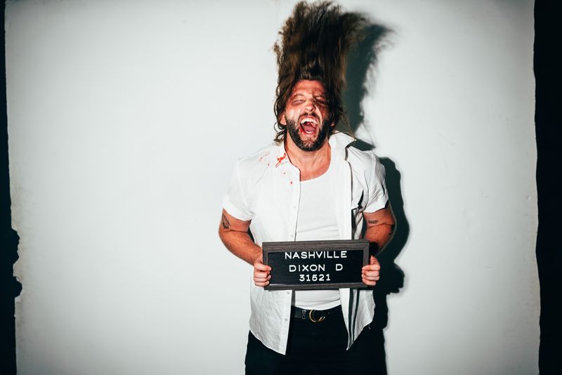 Mugshot placard, hair flung straight up, mid-scream under flash