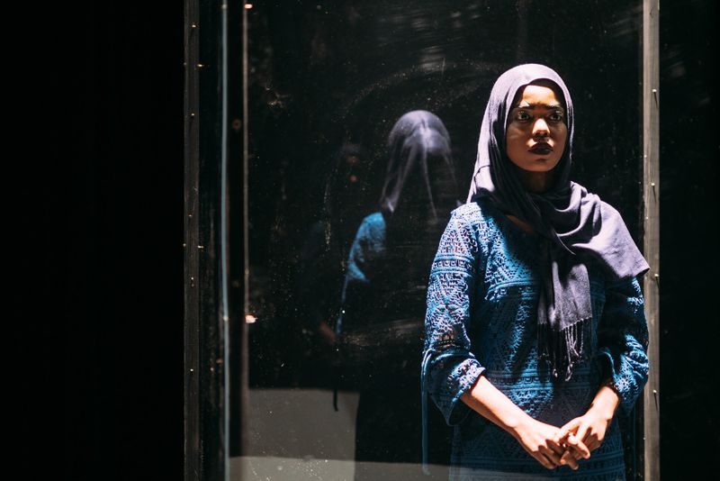 Woman in hijab inside glass case, her reflection beside her