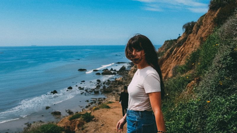 On a cliff above the Pacific, hair in the wind, a steady look, red earth and green slope