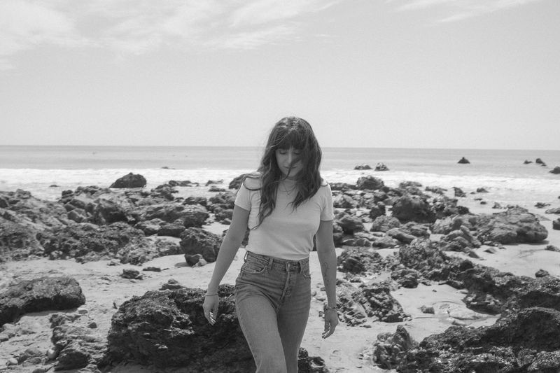 Black and white, she walks toward you, hair across her face, wet rocks