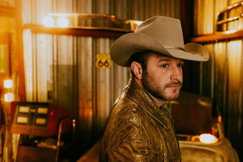 Cowboy hat, leather jacket, amber garage glow, Route 66 sign