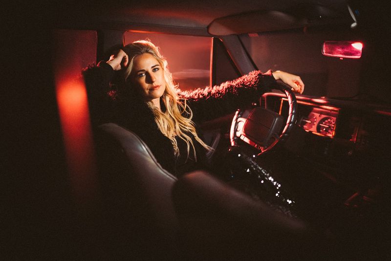 Red dashboard glow, reclining at the wheel, steady gaze
