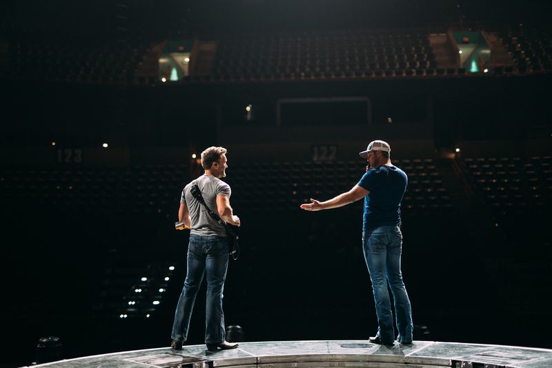Two figures talking on a lit round stage, dark empty arena