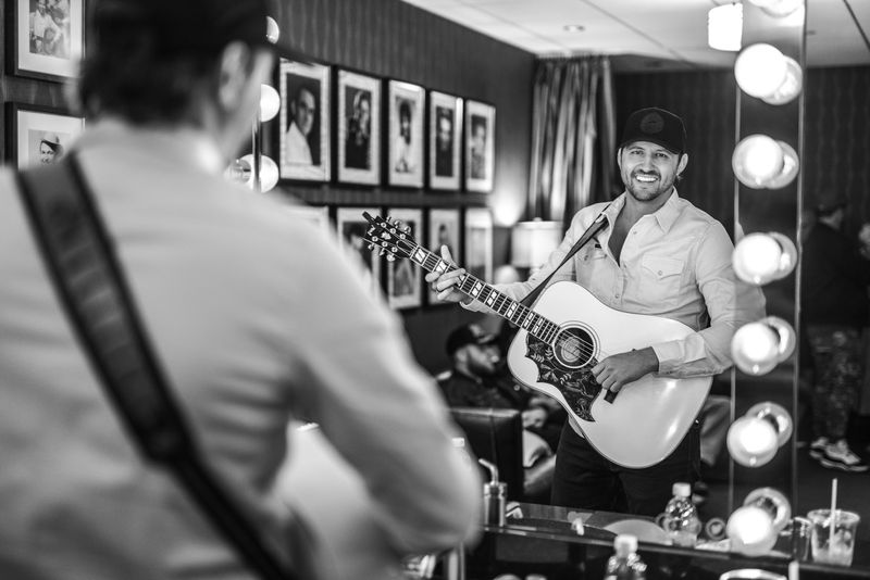 Beaming guitarist backstage, vanity bulbs and framed portraits, over-shoulder
