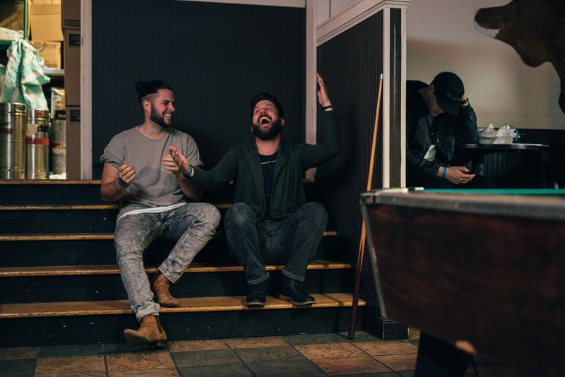Two men doubled over laughing on backstage steps