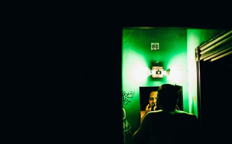 Green-lit mirror doorway in a black frame, face reflected