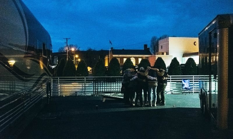 Band huddled between tour buses under deep blue-hour sky