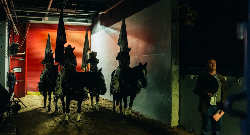 Flag riders backlit in arena tunnel, man waiting in side light