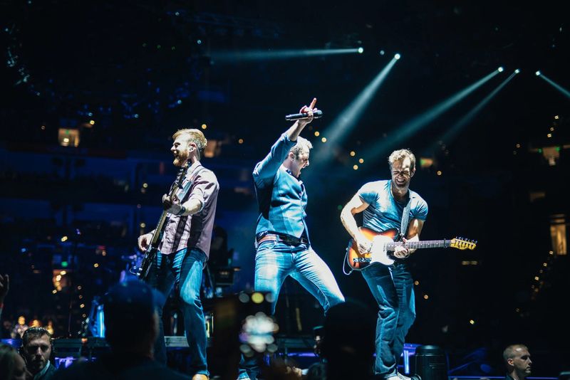 Three-man leap, mic pointed skyward, blue arena beams