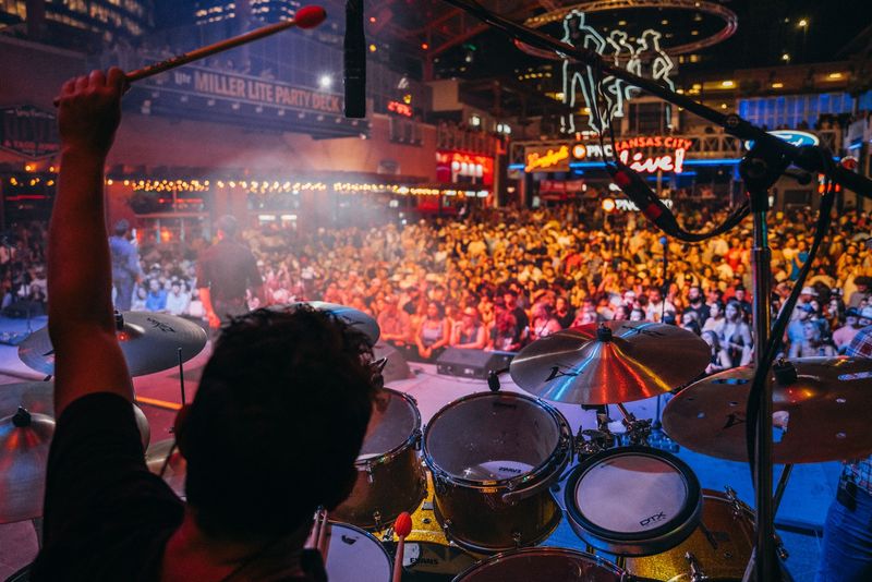 Drumstick raised over a packed neon-lit outdoor crowd