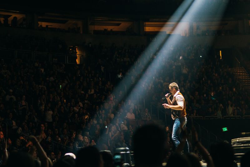 Diagonal spotlight beam cuts the arena, singer caught in it