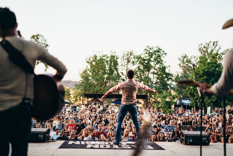 Arms flung wide to a packed outdoor crowd, from behind