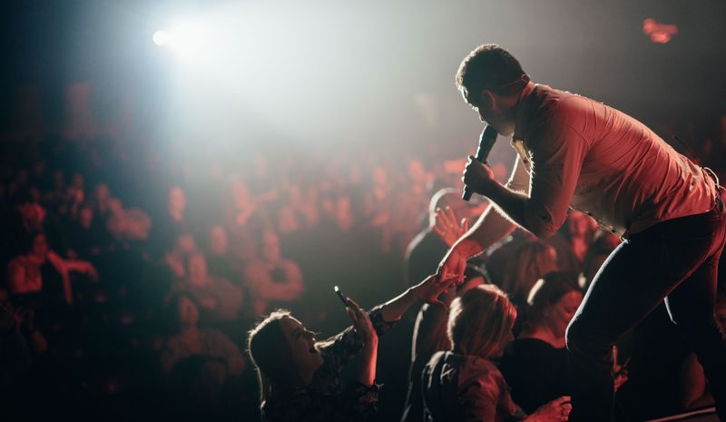 Singer leans into the crowd, hands reaching through backlit haze