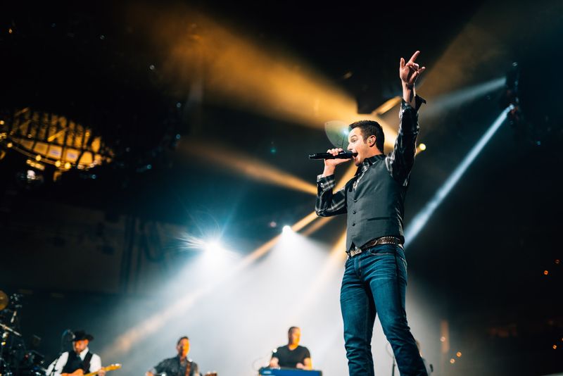 Arm thrust skyward, golden beams fanning across dark stage