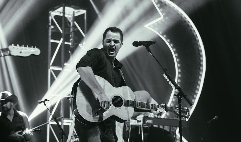 Full-throated shout over guitar, light beams fanning behind, black and white