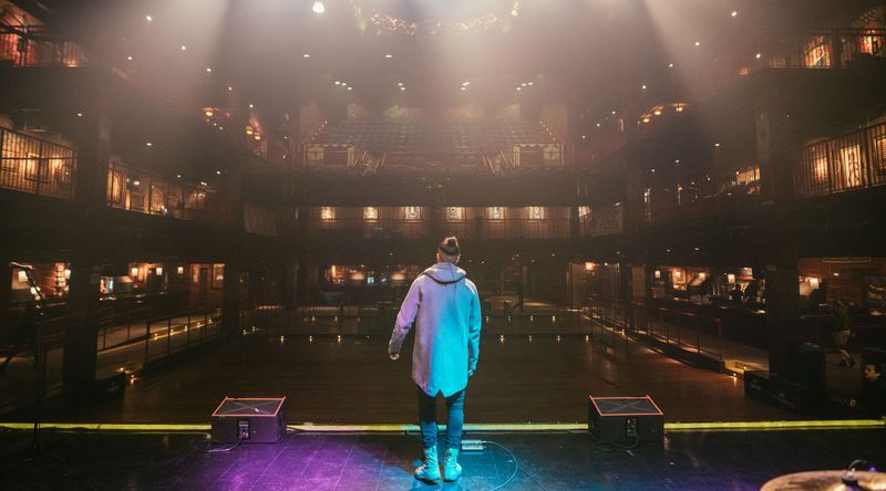Alone on stage facing an empty hazy theater, balconies glowing