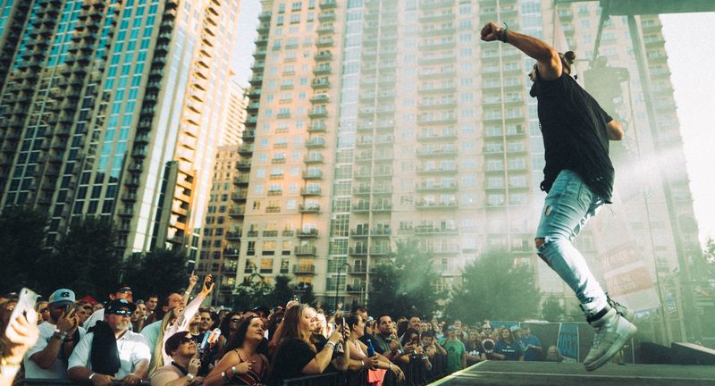 Performer airborne, fist raised, apartment towers rising behind