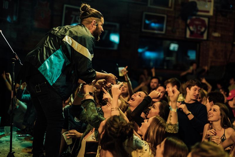 Performer leaning into screaming, reaching fans in a packed bar