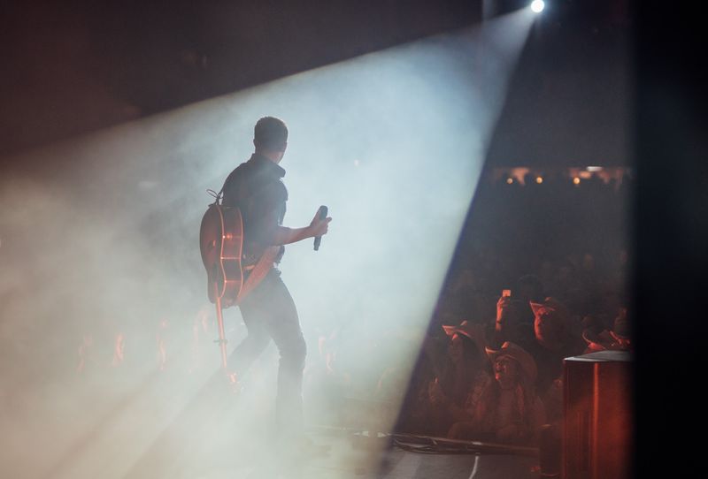 Guitarist striding through a huge diagonal spotlight beam