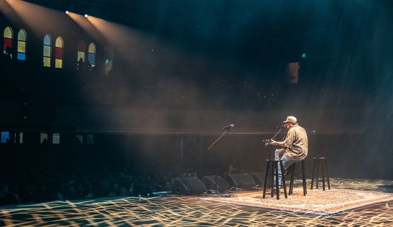 Lone singer on a stool, haze beams, stained glass behind